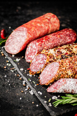 An assortment of delicious salami sausage on a stone board with rosemary. 