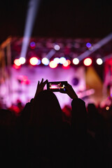 Person holding smartphone and silhouettes of concert crowd with stage lights