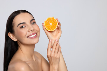 Woman holding half of orange on light grey background, space for text. Spa treatment