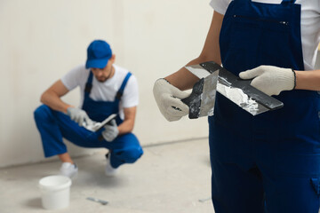 Professional workers with putty knives near wall indoors, closeup