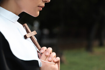 Young nun with Christian cross in park outdoors, closeup. Space for text