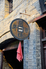 Vertical color image of an ancient Chinese shop facade with a huge metallic coin hanging on the wall
