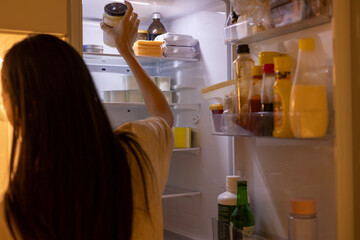 The woman is taking a bottle from the refrigerator in the kitchen