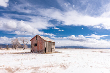 Red abandoned barn in an open field, San Luis Valley, Colorado, with fence, bright blue sky,...