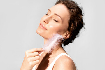 A woman with a white feather near her perfect facial skin, enjoying skincare cosmetics with her...