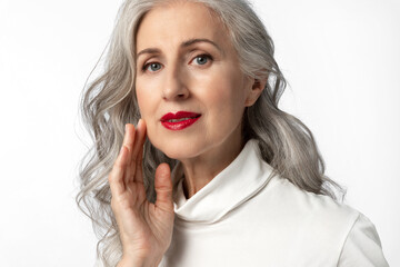 Portrait of a beautiful gray-haired woman with beautifully styled hair and natural makeup with red lipstick, looking at the camera with a gentle smile
