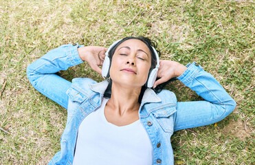 Music, headphones and woman relax in a park, peace and zen from above, content and calm. Podcast, earphones and girl resting while listening to audio for wellness, stress free and chilling on grass