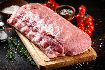 A piece of raw pork on a cutting board with tomatoes, spices and rosemary.