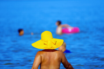 A woman in a hat watches children bathing in the sea