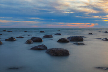 Fototapeta na wymiar Rocky shore of Baltic sea at sunset, sky is full of clouds, blue mood, long exposure. Viimsi, Estonia
