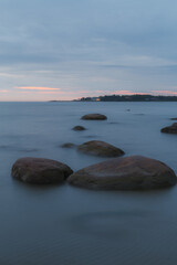 Blue hour after the sunset over rocky Baltic sea cost. Small stones and big boulders in the sea. Long exposure photo.