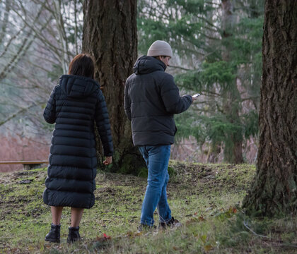 Man and woman walking in park looking at smart phones