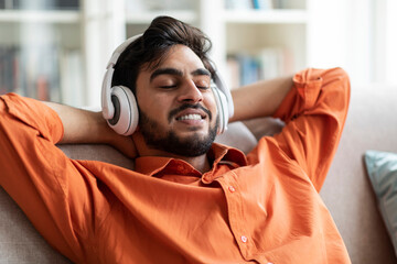 Happy middle eastern man resting at home, listening to music