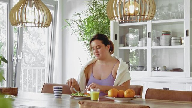 Waist up portrait view of the cheerful woman eating breakfast and smiling while enjoying