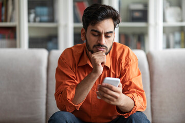 Thoughtful handsome middle eastern man using phone at home