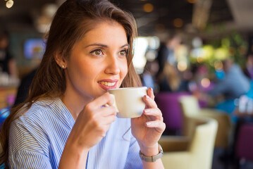 Young smiling woman drinking coffee in the coffee shop