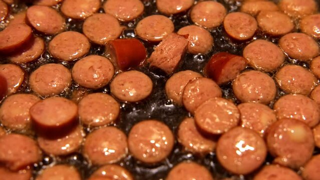 Slices of fried bangers in a frying pan. Farm, organic products. Homemade grilled pork barbecue sausages in an iron pan. Top view. Cooking Sausages. Roasted wurst, wiener. Full English breakfast. 4K
