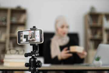 Focus on phone of muslim woman in casual wear and hijab recording video on smartphone while unpacking gift boxes. Female blogger sharing her emotions with her subscribers in social networks.