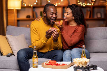 Happy young african woman feeding her boyfriend, home interior