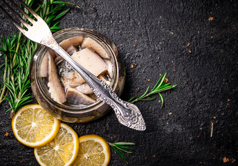 Pieces of salted herring in a jar with rosemary and lemon. 
