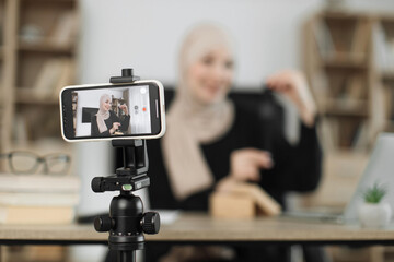 Focus on smart phone screen, muslim woman doing live stream while unpacking box with new smart watch. Female blogger sharing her feedback about modern gadget with her subscribers.