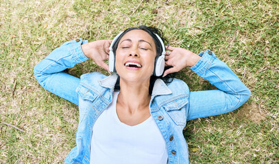 Music headphones, top view and woman relax at park outdoors. Peace, calm and happy, carefree and mature female streaming radio, podcast or audio song while relaxing or resting on grass in nature.