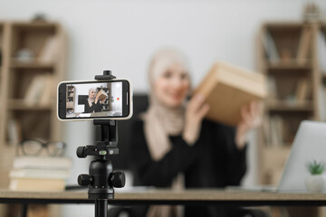 Focus on smart phone screen, pleasant arab woman filming video on modern phone camera while opening parcel box. Concept of people, technology and blogging.