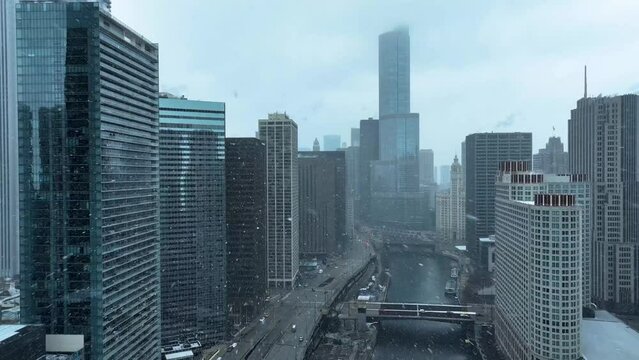 Drone aerial view of buildings flying over Chicago River pulling back toward Lake Michigan, snowing in winter on cloudy day
