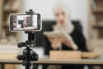 Focus on phone screen , muslim woman recording video on phone camera while unpacking box with new wireless tablet. Female influencer sharing with subscribers her positive feedback about new order.