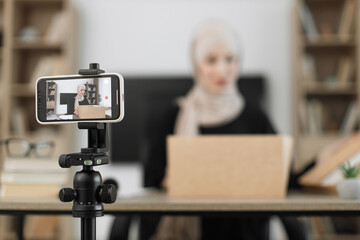 Focus on smart phone screen, pleasant arab woman filming video on modern phone camera while opening parcel box. Concept of people, technology and blogging.