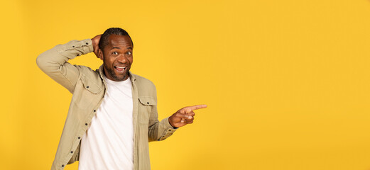 Cheerful surprised middle aged african american male in casual show finger to copy space, recommend...