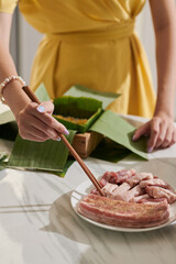 Woman using chopsticks when putting marinated pork in sticky rice cake