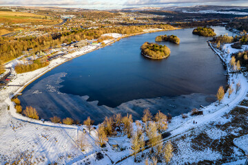 Aerial view of a freezing lake surrounded by snow in the South Wales Valleys (Bryn Bach)