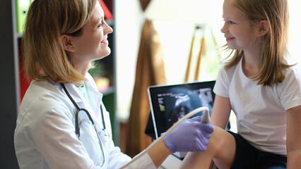 Female doctor makes ultrasound of knee of young patient in clinic.