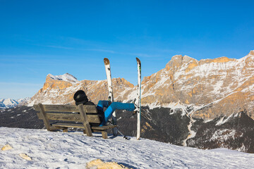 Skier resting on a bench overlooking the Italian Dolomites mountains. Ski, winter sport. Narciarz odpoczywa na ławce i podziwia włoskie góry Dolomity. Narty, sporty zimowe.