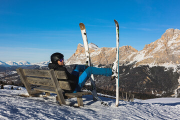 Skier resting on a bench overlooking the Italian Dolomites mountains. Ski, winter sport. Narciarz odpoczywa na ławce i podziwia włoskie góry Dolomity. Narty, sporty zimowe. © Anita