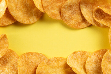 Potato chips scattered on the table close-up on a yellow background. Food with elevated cholesterol levels