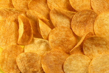 Potato chips scattered on the table close-up on a yellow background. Food with elevated cholesterol levels