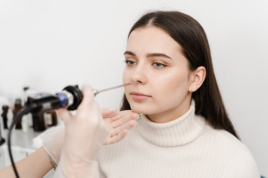 ENT doctor otolaryngologist with headlight treat nose woman patient. Nose endoscopy. Rhinoscopy procedure with rhinoscope.