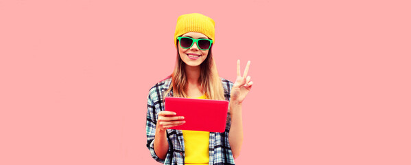 Portrait of stylish cool young woman model with tablet pc wearing colorful clothes on pink...