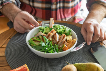 Man eating healthy dinner of grilled beef steak with vegetables, salad of green bean, peas and broccoli on wooden table at home
