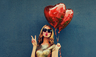 Portrait of happy young woman with red heart shaped balloons blowing her lips on dark background