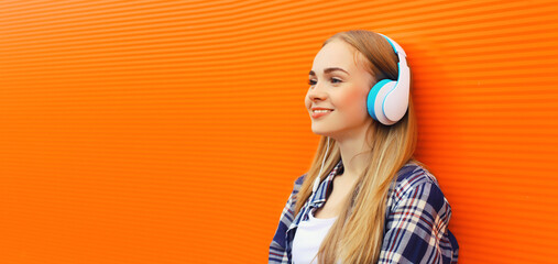 Portrait of happy young woman in headphones listening to music on colorful orange background