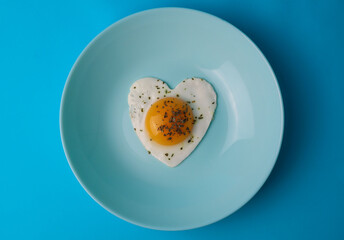 on a bright blue background, a light blue plate in which a hearty breakfast in the form of scrambled eggs with a bright yolk in the form of a heart