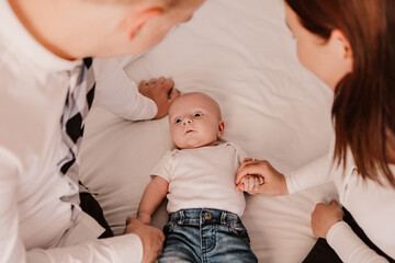 Fototapeta na wymiar Little boy cute child baby playing with parents. Toddler lying on bed having fun dressed blue jeans and white t-shirt. Happy childhood, family concept 
