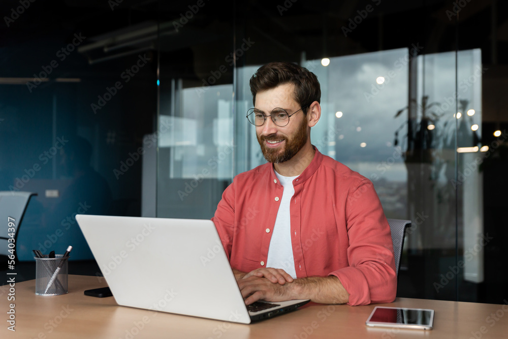 Wall mural successful smiling man working inside office with laptop, businessman in red shirt smiling and typin