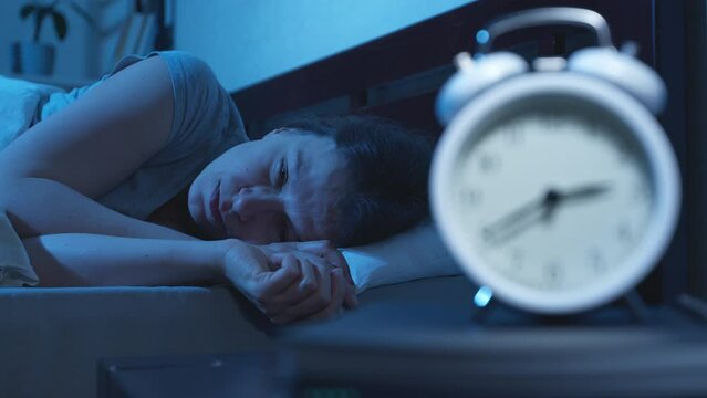 Insomnia. A woman cannot sleep at night lying on the bed. Clock in the foreground.