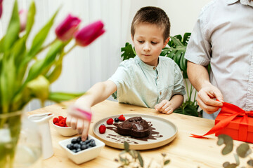 Dad and son decorate a heart-shaped cake with fresh berries and prepare a gift. Mother's Day, International Women's Day, Valentine's Day