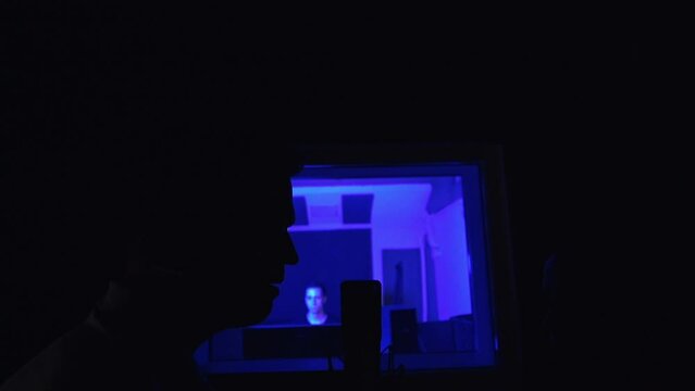 Dark silhouettes of male and female singers in front of the microphone in a dark room. Studio for professional music recording indoors.