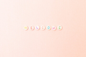 Word Welcome. Quote made of white round beads with multicolored letters on a pink glittering background.